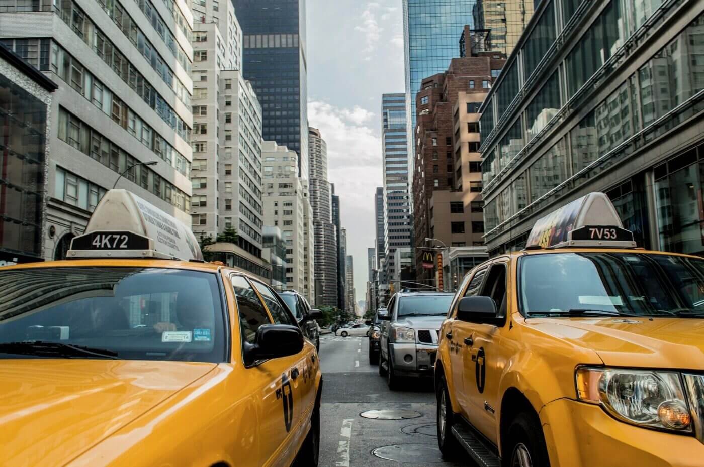 A congested city street filled with vehicles, ranging from sedans to delivery trucks, creates a chaotic scene beneath a backdrop of tall buildings. The sidewalks are crowded with people, some hurrying while others appear to be waiting, emphasizing the high population density. The urban environment is vibrant but also demonstrates how quickly resources like fuel, food, and water could become scarce in a crisis. The image highlights the critical need for emergency preparedness, alternative transportation options, and sustainable living strategies in such a crowded setting. It serves as a visual reminder of the potential challenges of navigating an urban landscape during disasters.